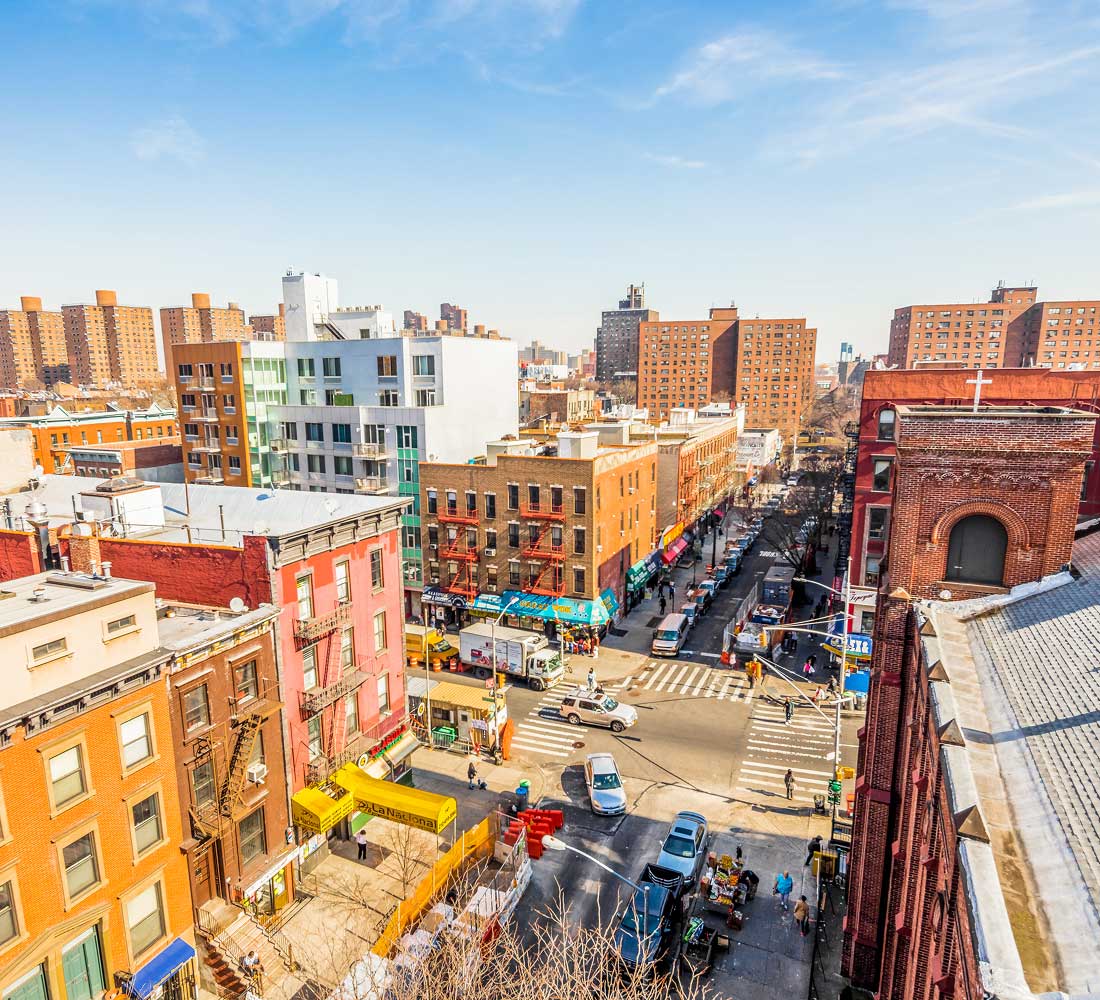 Intersection of Harlem streets with brightly colored buildings of different heights, cars, and pedestrians