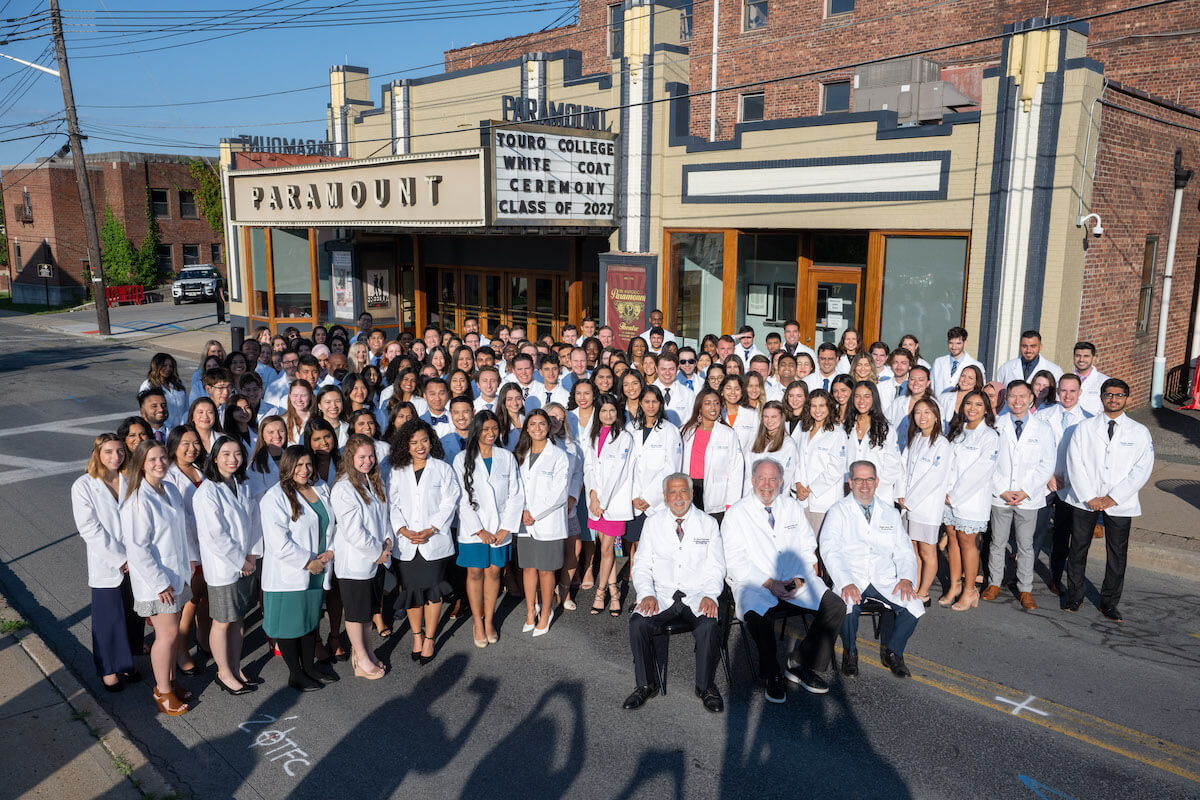 Osteopathic medical students stand in white coats before a theater in Middletown, NY.