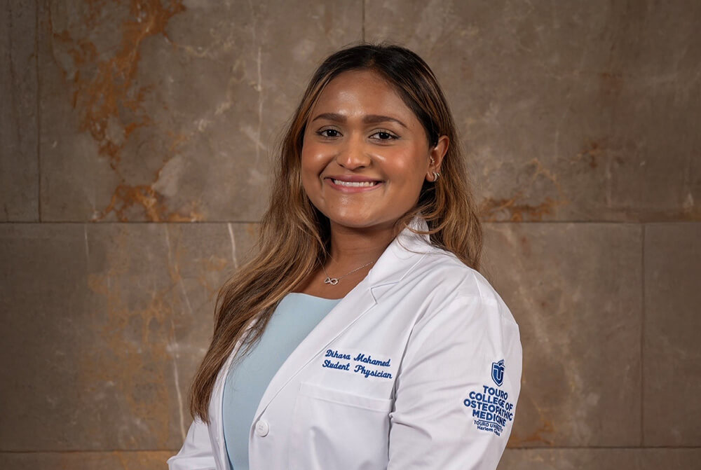 Young woman standing sideways smiling at camera wearing her doctor\'s "white coat" 