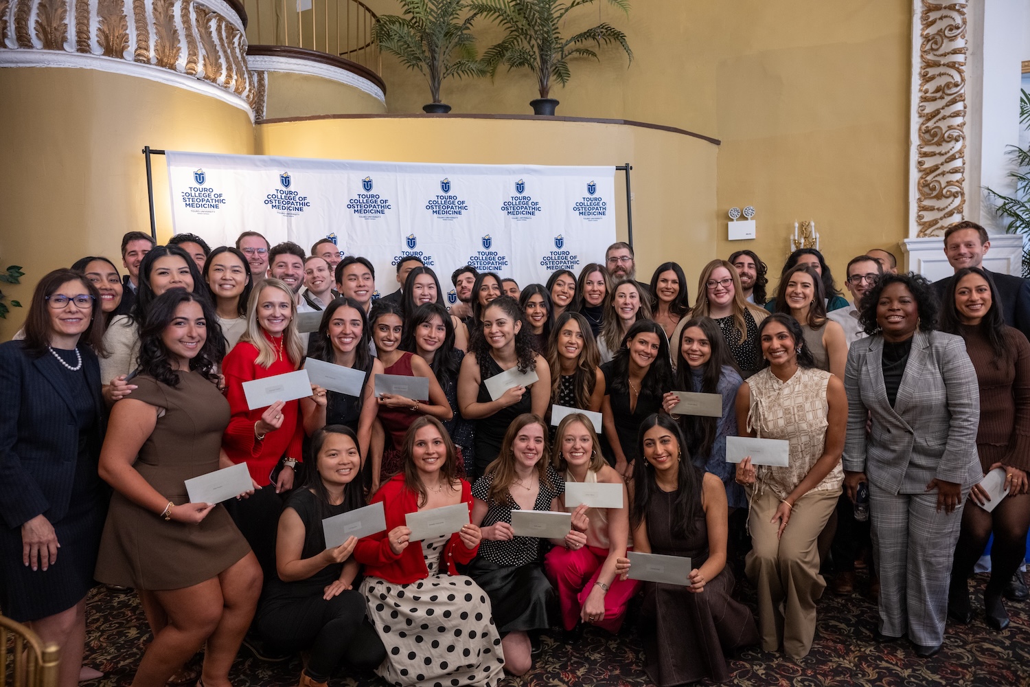 Male and female medical students huddle in a group, smiling and excited, against a backdrop minutes before learning where they will go to begin residency. 