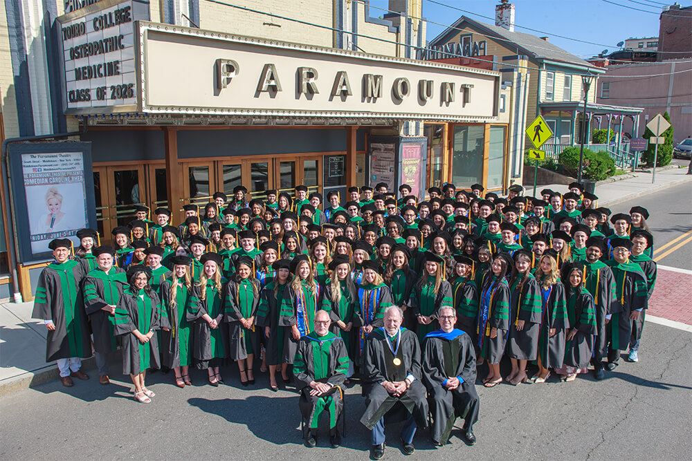 Touro College of Osteopathic Medicine Class of 2026 standing with faculty members outside the Paramount Theater in Middletown, NY.