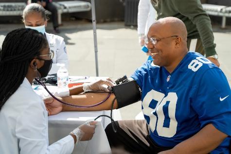 Female medical student taking blood pressure of male at Harlem health fair. 