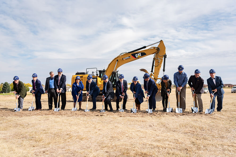 Touro and Benefis executives lined up in front of an excavator, each holding a shovel, for Groundbreaking at Touro College Montana