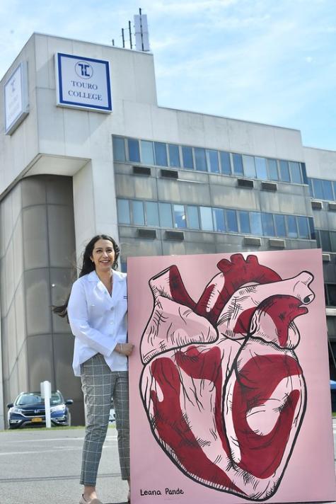 woman standing outside in front of school building next to her stylized painting of a heart
