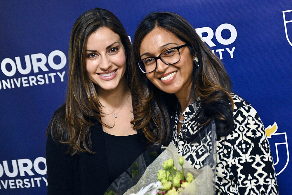 two women standing and smiling at camera holding bouquet of flowers 