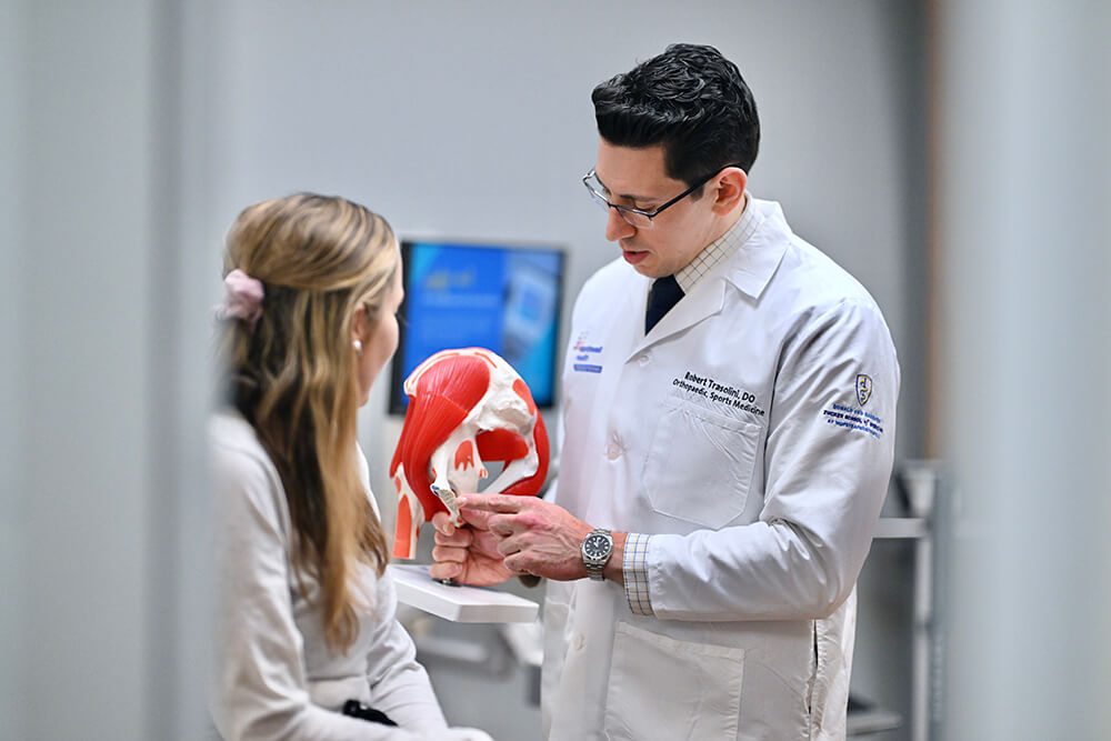 Orthopedic surgeon Dr Robert Trasolini points to something on medical muscular model to explain procedure to female patient