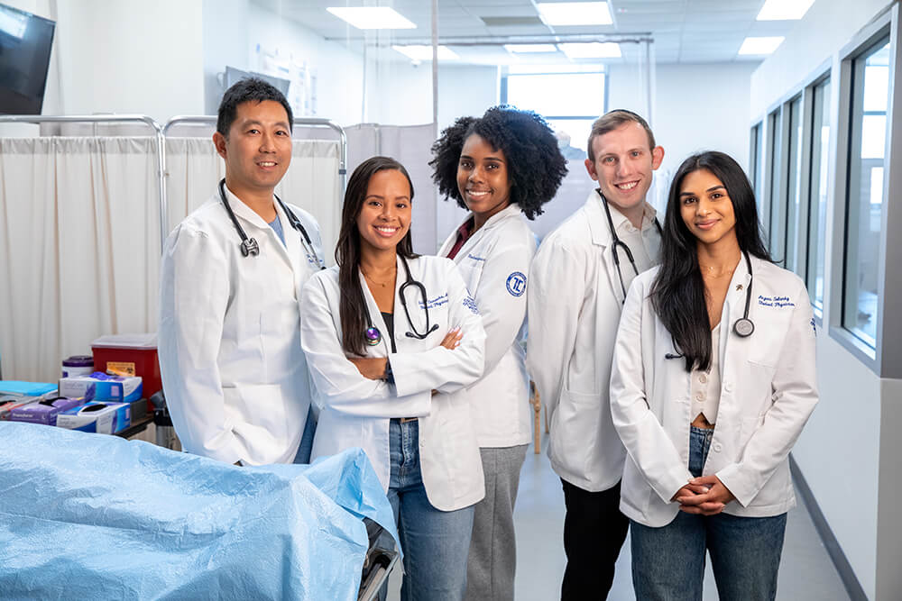 Male and female medical students standing and smiling in a line together in a medical school lab. 