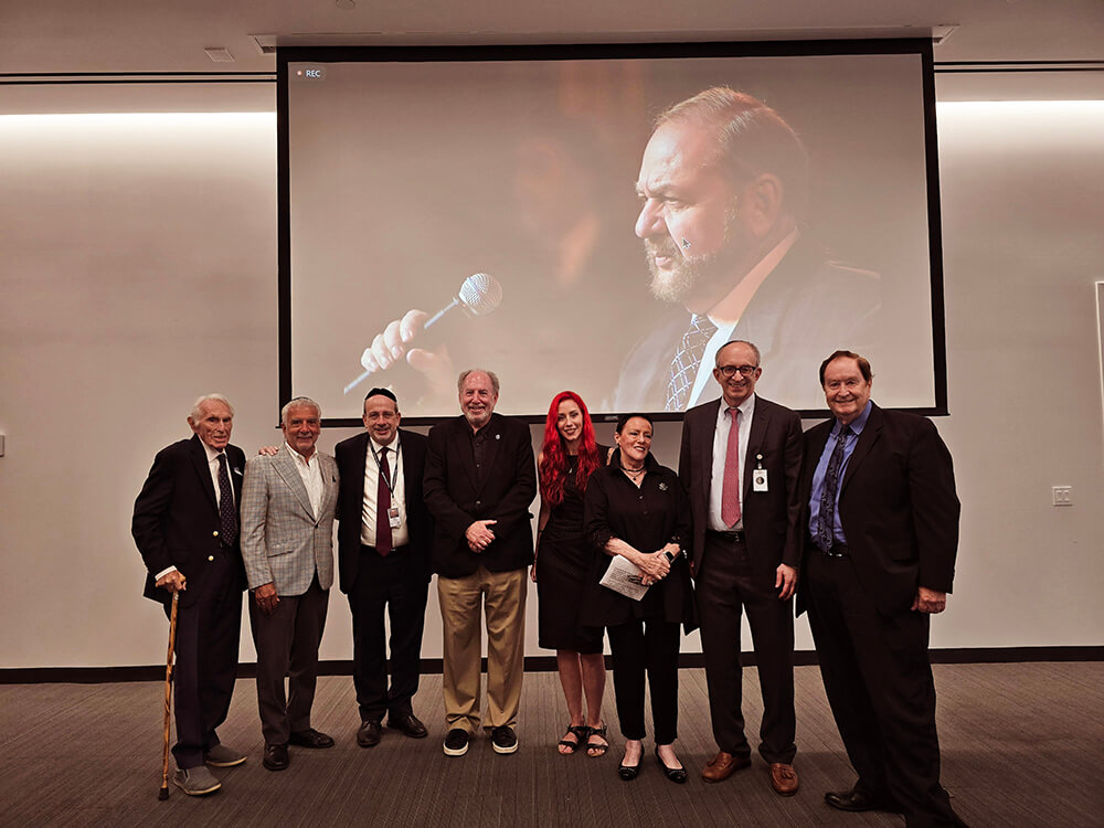 Group of men and women standing front of memorial event for Dr. Jay Sexter facing audience. 