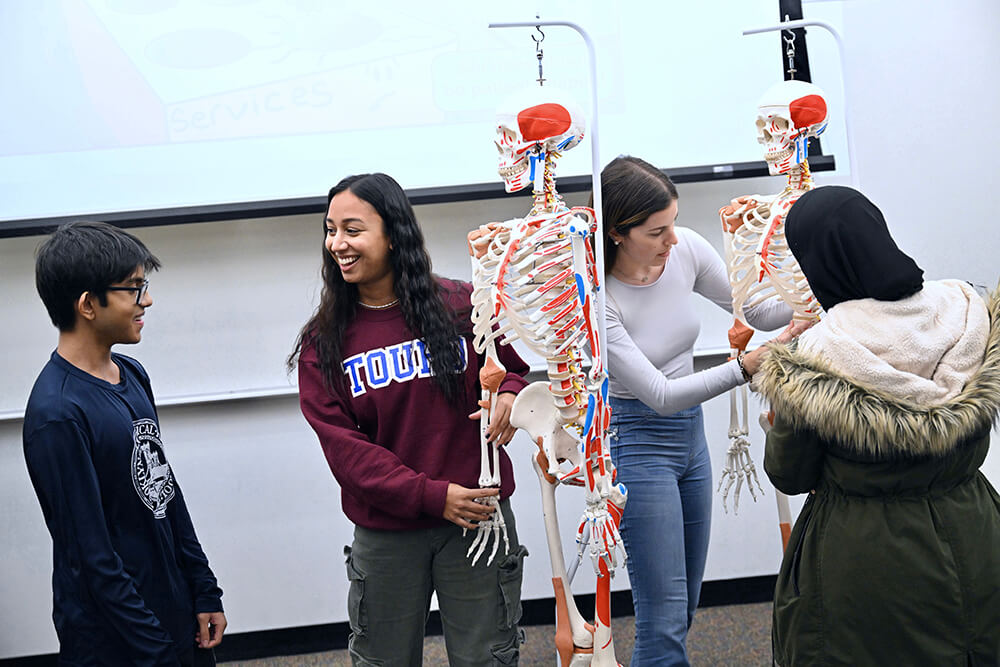 2 female high school students working with medical skeletons and talking to another male and female students