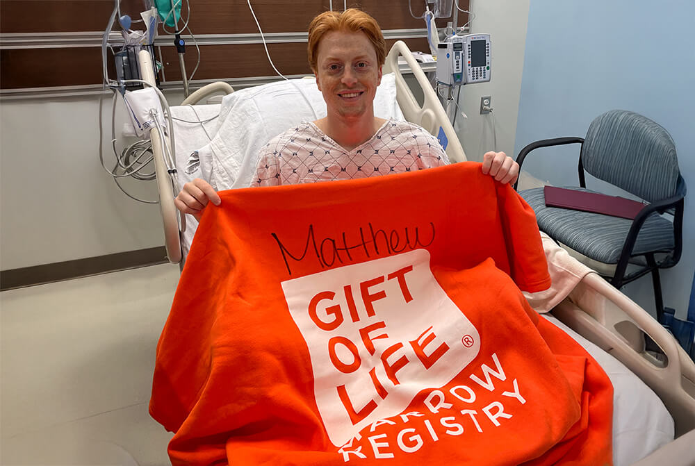 Young man sitting up in hospital bed smiling after donating his bone marrow to help save a toddler\'s life.