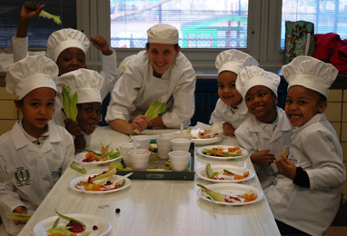 Children dressed in chef clothing sit by a table