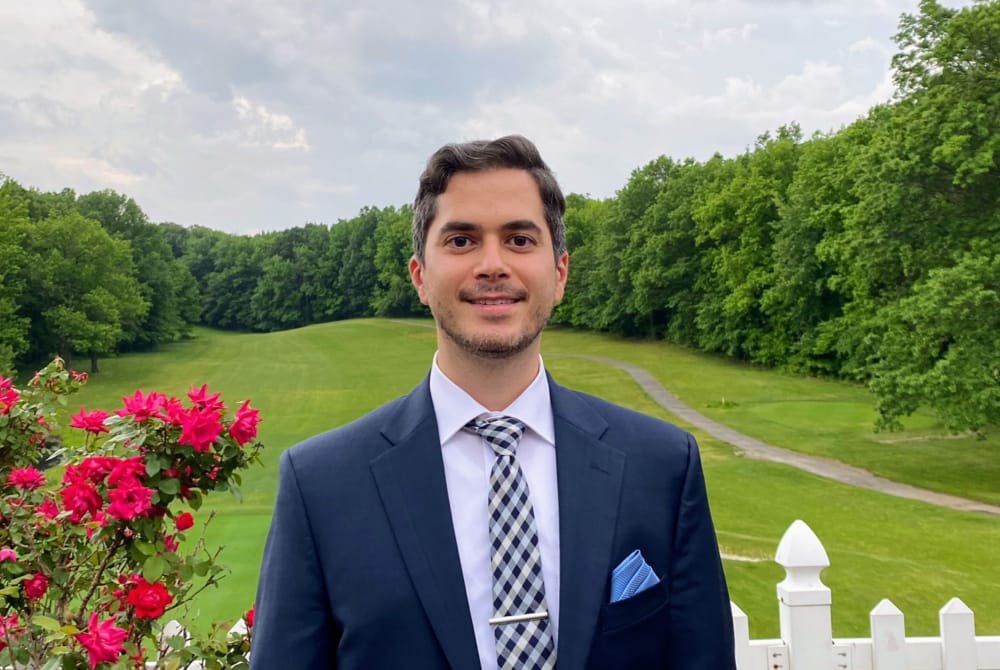 Chaim Poper posing in front of a white picket fence and rosebush